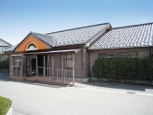 グレーの屋根が付いた平屋建ての建物がある敷地内には緑も植えられ、玄関には屋根が付いている。