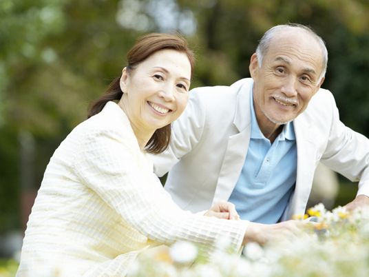 こちらを向いて優しく微笑んでいる高齢者夫婦。広い公園のような場所