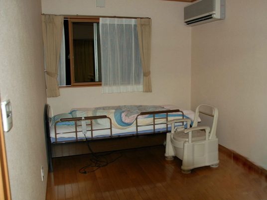 ポータブルトイレを設置したフローリングの部屋にはエアコンや寝具付きのベッドが付いている。