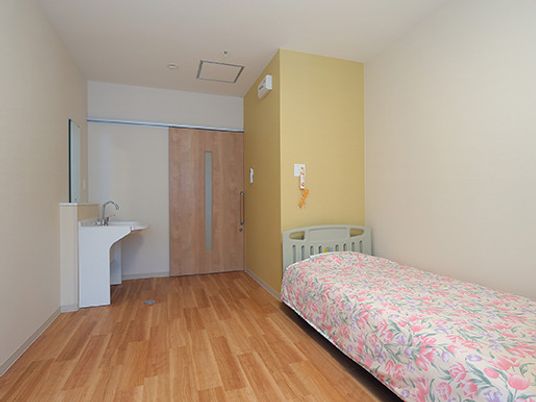 車いす対応の洗面所が付いたフローリングの部屋には寝具付きのベッドが置かれ、緊急通報装置もある。