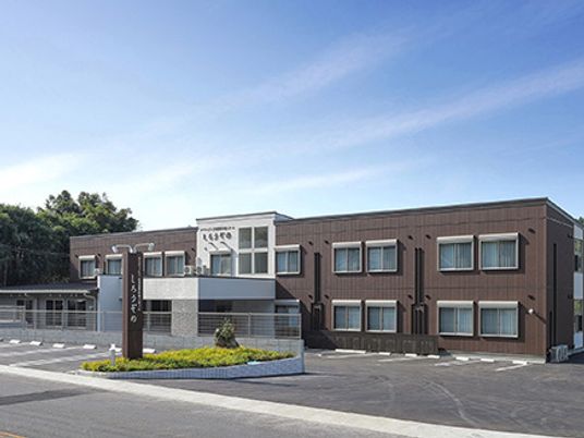 ブラウン系の外壁の２階建ての建物は日当たり良好で建物の前には駐車場もある。
