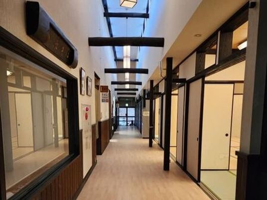 天井の高い建物内の廊下は幅が広くまっすぐで、右側には和室が並んでいる。防災設備も設置されている。