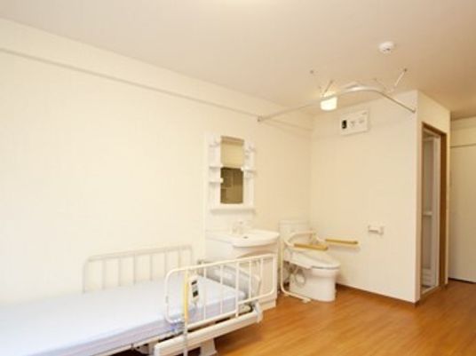 介護ベッドが置かれたフローリングの居室にはトイレや洗面所があり、家具などは置かれていない。