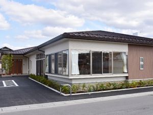 平屋建ての建物は落ち着いた色合い。駐車場が付き、建物の周りには木が植えられている。