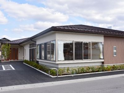 平屋建ての建物は落ち着いた色合い。駐車場が付き、建物の周りには木が植えられている。