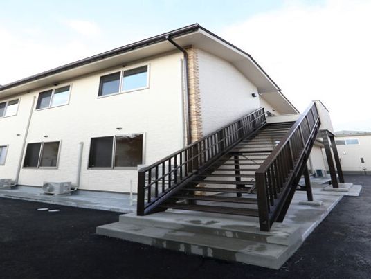 屋外階段が設置されたベージュ系の２階建ての建物には屋根があり、窓もたくさんついている。