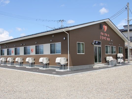 ブラウン系の平屋建ての建物は三角屋根で、玄関先には階段とスロープがつけられている。