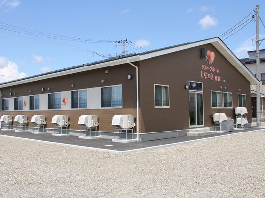 ブラウン系の平屋建ての建物は三角屋根で、玄関先には階段とスロープがつけられている。