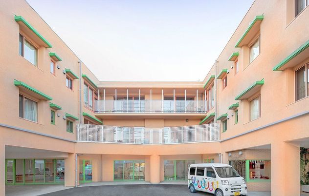 コの字型のオレンジ系の外壁の３階建ての建物の前には車が止まっている。