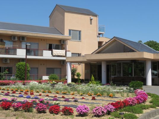 花壇には色鮮やかな花がたくさん植えられていて2階建てのブラウン系の建物にはベランダもある。