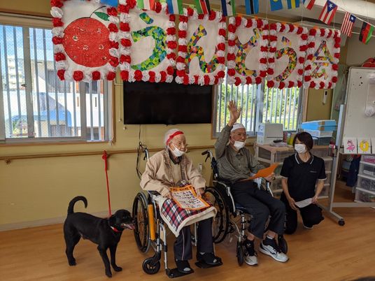 車いすに座っている男性と女性、黒い犬、女性スタッフ