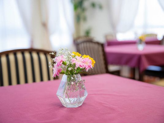 小さなガラス製の花瓶には、黄色とピンク色の２種類の花とカスミソウが束ねられている。テーブルの上に飾られている。