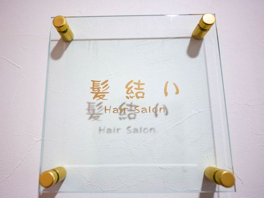美容ルームであることが透明ガラス板に表示されている。文字は金色で書かれていて、金色のビス４つで壁に設置されている。