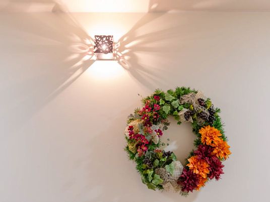 色とりどりの草花で編み上げられた大きなフラワーリースが、小さな間接照明を受けて白色の壁面に飾られている。