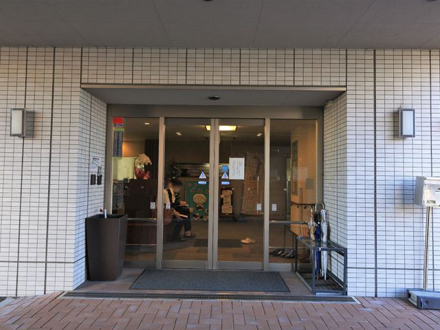入口のある清潔なエントランス 玄関 ガラス扉を配したエントランスは明るく迎え入れる雰囲気です。働くスタッフの姿も見え、安心感を与える空間となっています。
