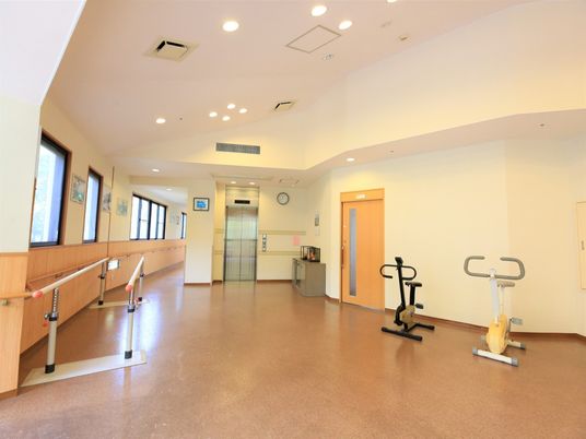 機能訓練室には平行棒をはじめ、筋力を高めるための運動器具が設置されている。長い廊下と繋がっているので、歩行訓練も可能である。