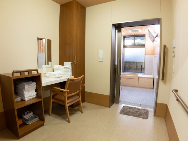 居室の一部と廊下 脱衣所  清潔感のあふれる居室と廊下は、余裕を持った造りでくつろげる設計です。タオル類が整えられた棚や、使いやすい高さのテーブルが配置されており、日々の快適さが考えられています。
