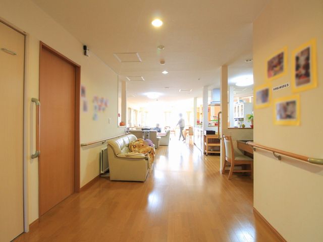 共有スペースの廊下と空間 通路 明るく広々とした廊下には、手すりが備わり、壁には活動の写真が飾られています。職員の方が遠くで仕事をしている様子が見て取れます。
