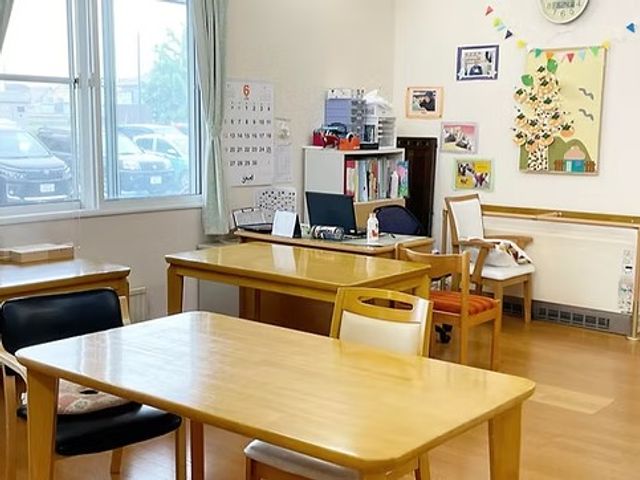 明るい共有スペース リビング   窓から自然光が入る、木目調の家具が並ぶ明るい共有スペースです。座って過ごしやすい落ち着いた雰囲気が感じられます。