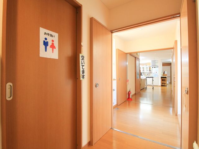 明るい廊下と扉 トイレ ゆったりとした通路が、明るく開放感のある作りになっていて、誰もが快適に過ごせる環境が整っています。扉の向こうには、共用スペースが見え、日々の業務の効率も良くなりそうです。