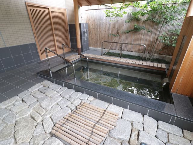 和風の美しい浴室空間 露天風呂 手すり付きの浴槽と緑あふれる景観が特徴の憩いの空間です。日々の疲れを静かに癒す時間をご提供します。