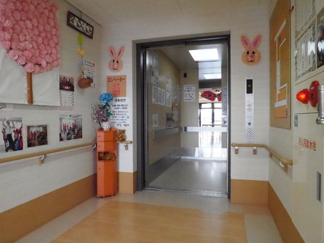 エレベーター前の廊下 エレベーター 装飾が施された廊下です。壁には掲示物や写真が飾られ、温かみのある雰囲気を感じられる空間になっています。