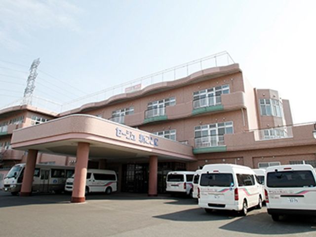 建物正面と車両の外観 外観   広いひさしのある正面玄関が目立つ建物です。送迎車が停まっており、出入りのしやすさがうかがえます。