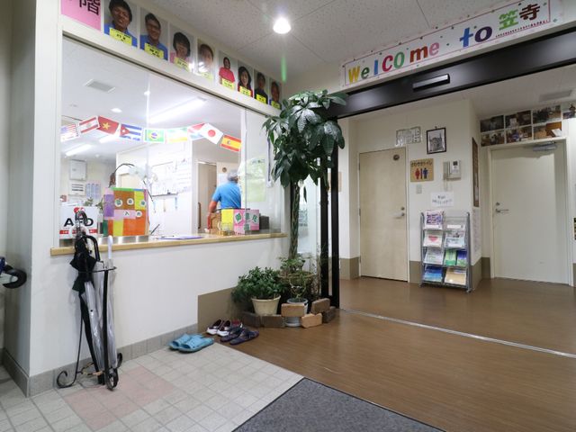 受付と掲示物のあるエントランス 受付 アットホームな雰囲気の受付スペースです。スタッフの方が入退所者の対応をされており、植物も飾られています。