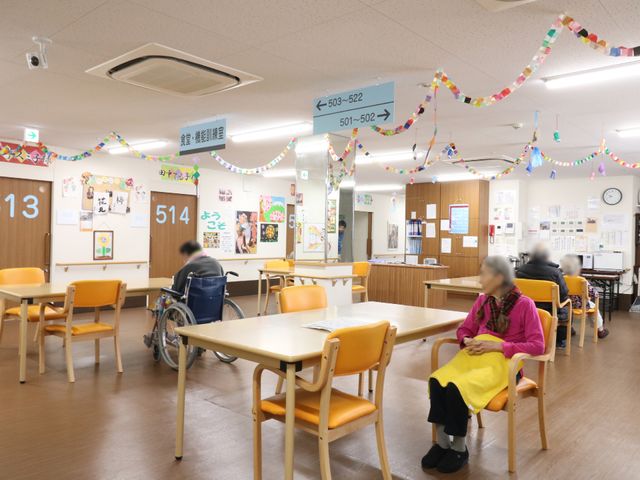 飾り付けされた明るい食堂 多目的スペース2. カラフルな装飾が施された食堂で、利用者の方々がリラックスした様子でくつろいでいます。車椅子を利用している方もスムーズに移動しており、共に温かな雰囲気が感じられます。