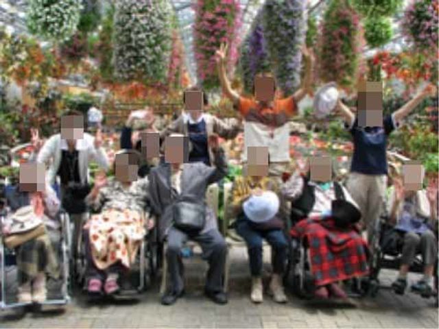 椅子に座る人々と花 外出イベント 様々な花々に囲まれた憩いの場所で、利用者の皆さまが楽しげな様子で談笑しています。自然の中でのリフレッシュも、就業の一環となります。