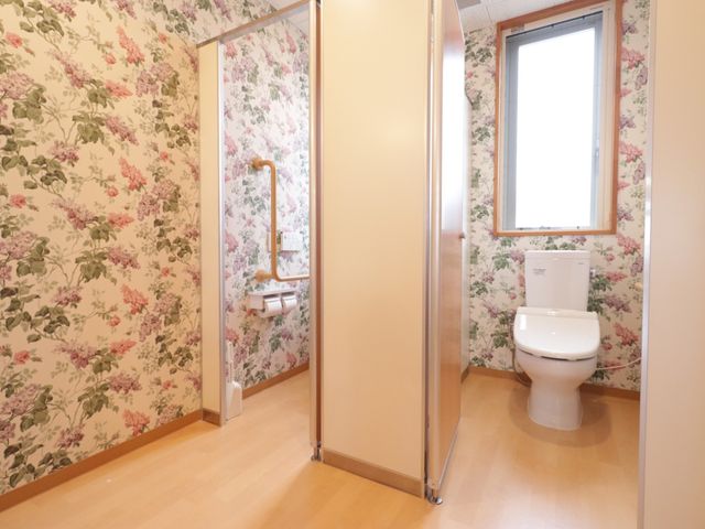 花柄壁紙のトイレ空間 トイレ 落ち着いた花柄の壁紙が特長的な明るいトイレ空間です。手すり設置で安全性も考えられており、どなたにも使いやすい環境を整えています。