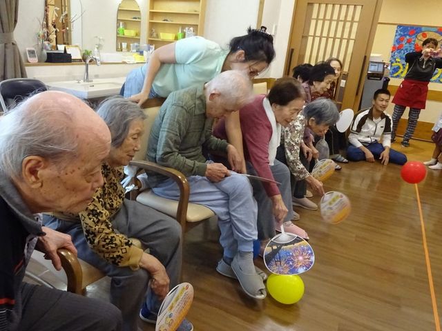 活動する高齢者の様子 レクリエーション 笑顔あふれる明るい雰囲気の中で、利用者様が楽しみながら機能訓練に取り組んでいます。スタッフの手厚いサポートも感じられますね。
