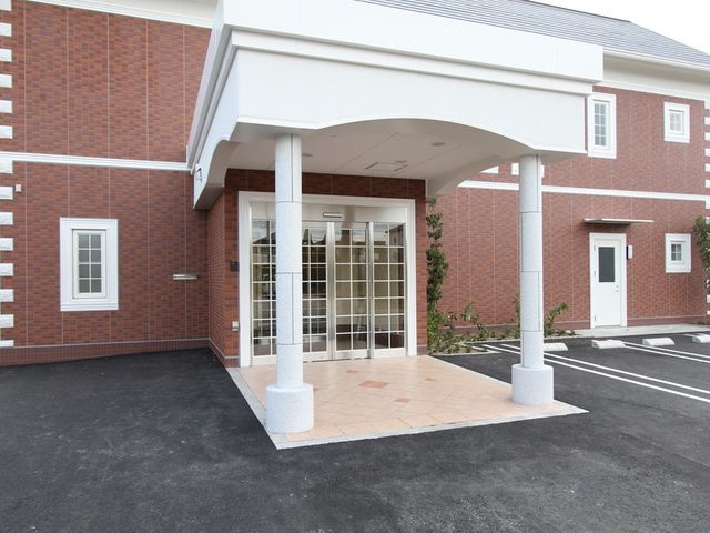 建物の正面玄関 外観   赤レンガ調の外壁に、屋根付きの出入口が設けられています。車寄せのある落ち着いた正面玄関です。