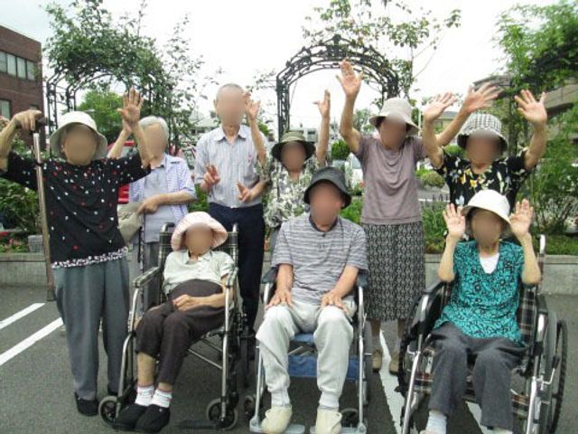 手を挙げる笑顔の集まり 日常 広々とした外の空間で、ご利用者が明るく手を挙げている様子が伝わります。外の新鮮な空気を感じながら、日々のリフレッシュが可能です。