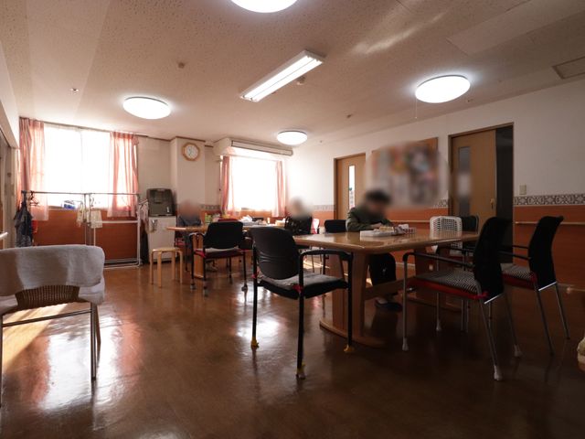 共有スペースの明るい居室 リビング 広くて温かみのあるダイニングルームです。職員が優しく対応しており、入居者が心地よい食事時間を過ごしています。