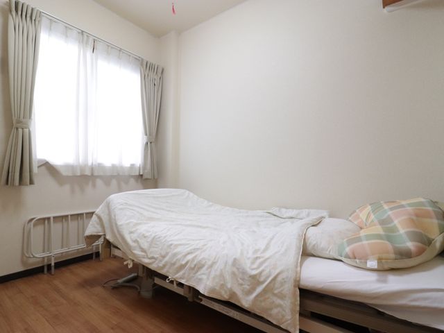 居室の明るい空間 ベッド 窓からの自然光が差し込む居室です。シンプルで清潔感のある設計が、くつろぎの時間をサポートします。