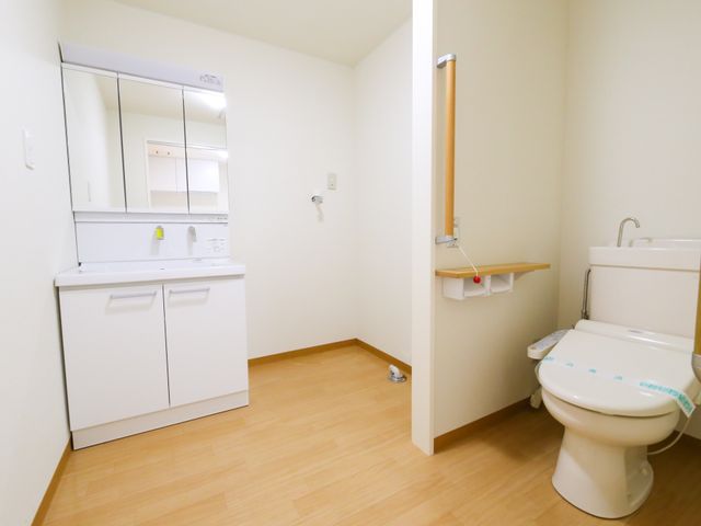 清潔なトイレと洗面台 居室 広々として清潔感のあるトイレ空間です。手すりが設置されており、安全に配慮された環境が整っています。