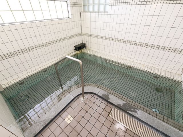 清潔感のある浴室 大浴場 手すりを設置した、広々とした白いタイルの浴室です。安全に配慮された設計で、心地よいバスタイムを過ごせます。
