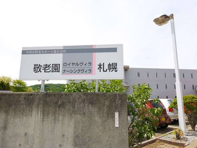 施設入口看板の映像 施設看板 訪れる方を迎える入口看板が設置されており、清潔感のある施設の外観が見えます。この施設で働くことを検討されている方には安心の環境です。