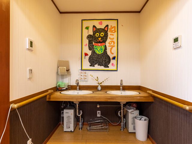 手洗い場の壁画と設備 洗面台 手すり付きの洗面台は、利用者の使いやすさを考慮した設計です。壁には心温まる色鮮やかな壁画が飾られ、明るい雰囲気が漂います。