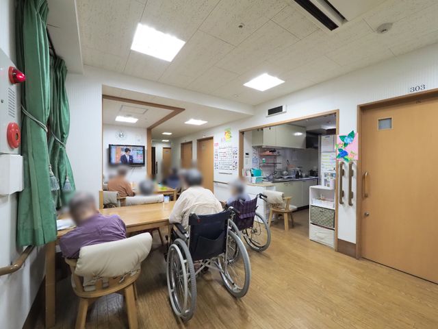 共有ダイニングエリア リビング 椅子に座ってテレビを見ている方々がいる居心地の良いダイニングです。キッチンには作業スペースがあり、利便性を考慮しています。
