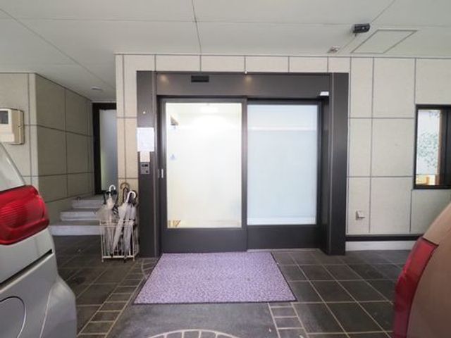 入口の自動ドアと傘立て エントランス 広々としたエントランスが、ご訪問の際の快適な第一歩を約束します。自動開閉の扉で、手をふさがない移動が可能です。