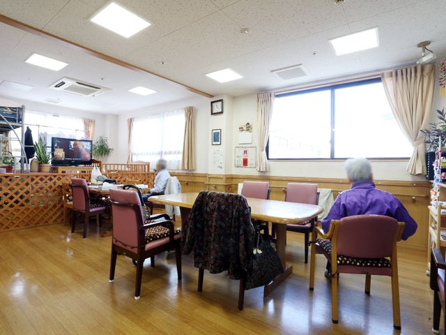 明るい共有ダイニング空間 リビング ゆとりを感じるダイニングルームで、利用者の方々がリラックスしながら食事や会話を楽しんでいます。天井の高い採光が素敵な空間を演出しており、快適な就業環境が期待できます。