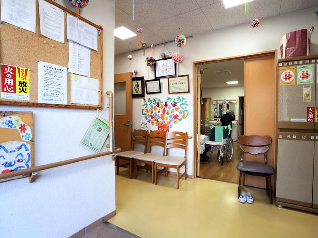 廊下と開いた扉の風景 廊下のスペース 温かみのある廊下は、掲示版や美しい手作りの飾りで彩られ、入居者様が日々の様子を共有しています。ゆったりとした通路が、快適な移動をサポートしています。