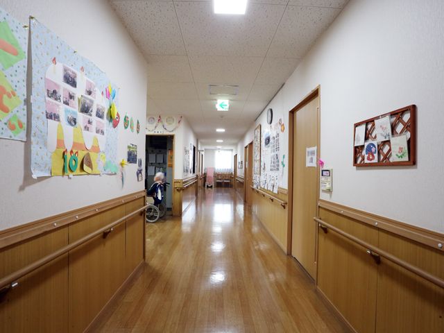 廊下に飾り付け 長い廊下 壁には季節の作品が飾られ、温もりを感じる廊下を一人の利用者が静かに過ごしています。滑りにくい床で安心です。