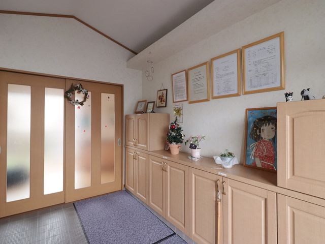 エントランスの受付コーナー 玄関 温かみのある木目調のエントランスには、来訪者を迎える笑顔があり、安心感を与える空間が広がっています。装飾も季節を感じさせ、訪れる方々を優しくもてなします。