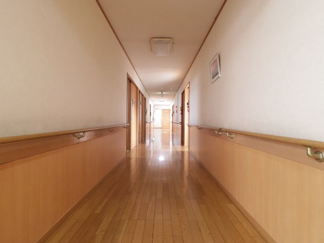 明るい廊下の風景 通路 清潔で明るい廊下が広がっており、手すり付きで安心して歩ける環境が整っています。ここで働くことで、快適な空間を提供できる喜びを感じられます。