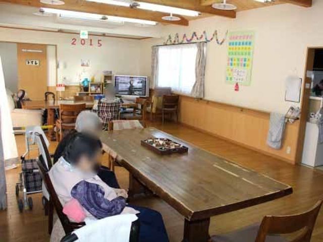 居心地の良い居室空間 リビング 天井が高く、自然光がたっぷり差し込む居室です。ゆったりとテレビを観る方の姿が見え、温かみのある雰囲気を感じられます。