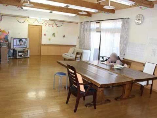 温かみのある居室空間 リビング ゆったりとした木のテーブルが中心の居室です。椅子に座った方が窓際でリラックスしながらくつろいでいます。
