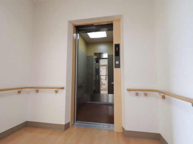 明るい廊下とエレベーター エレベーター 広々とした廊下には手すりが整っており、エレベーターもスムーズにアクセス可能です。働く環境としても、日々の業務がしやすい設計になっています。